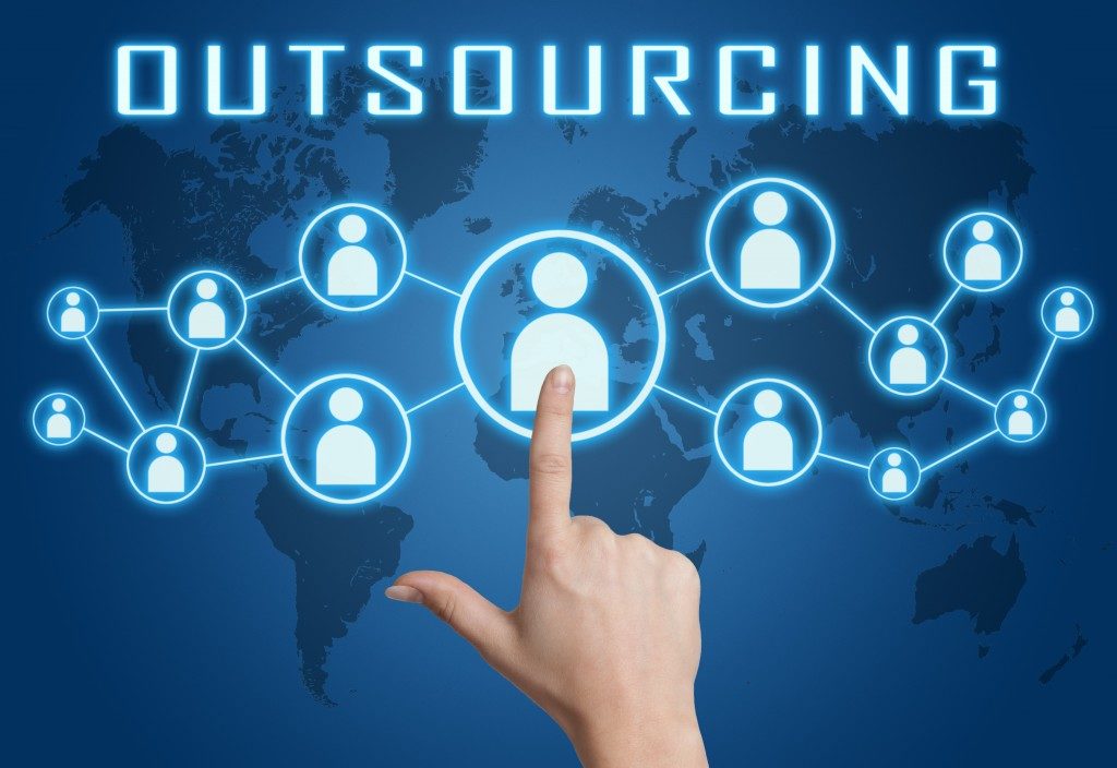 Outsourcing concept with hand pressing social icons on blue world map background