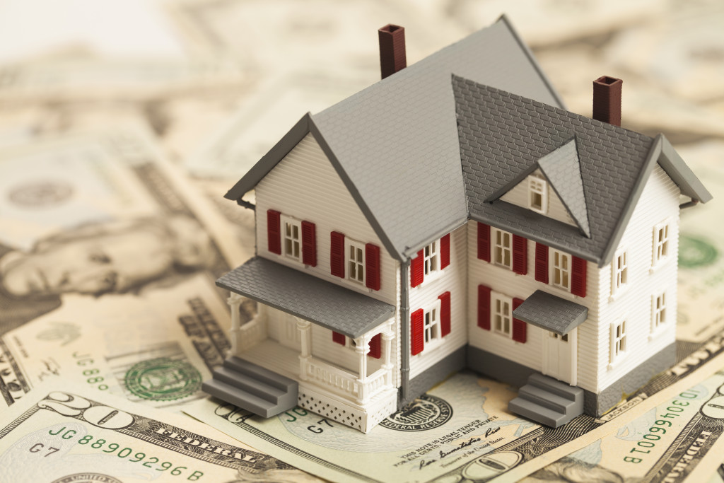 miniature house model on top a pile of dollar bills to represent property investment
