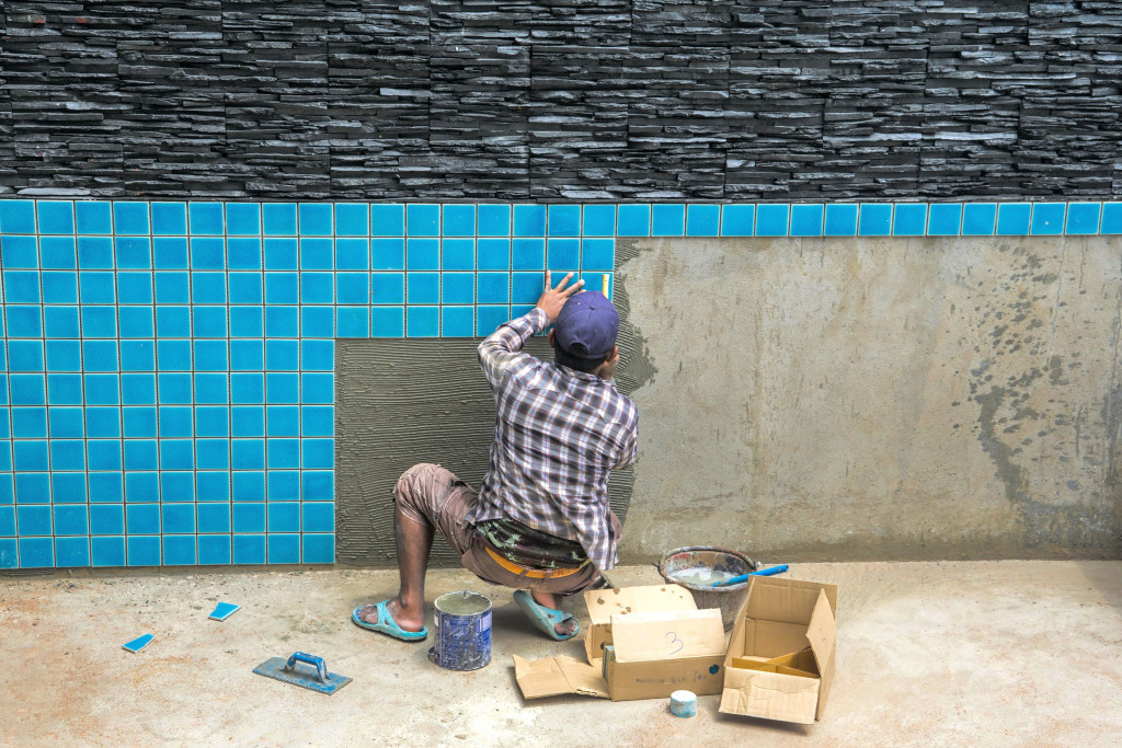 A man installing blue tiles for pool construction