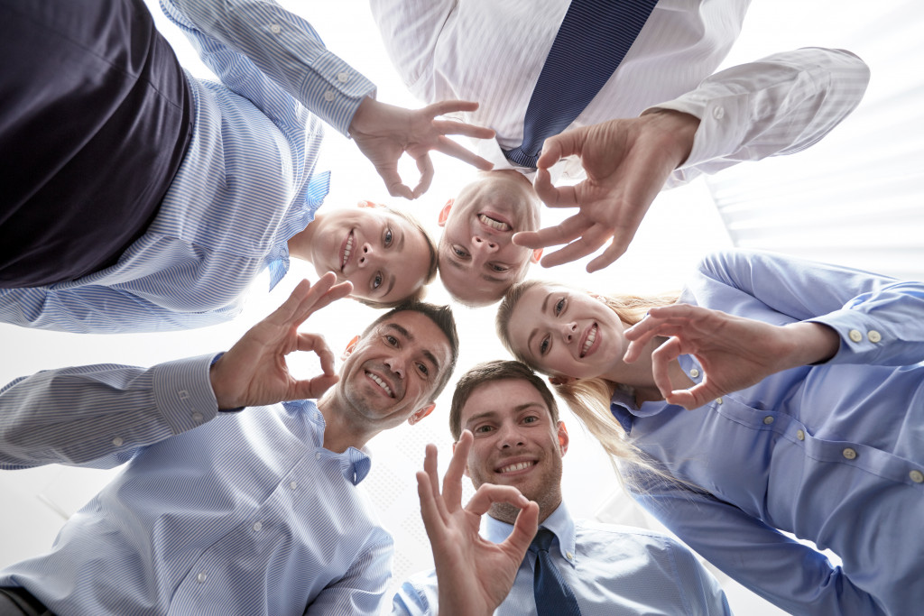 five employees looking at the camera below them doing an okay sign