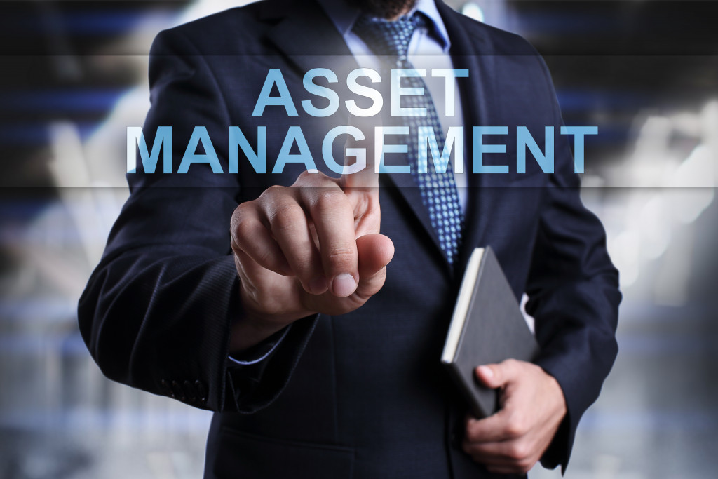 a businessman touching the word asset management while holding a gray book