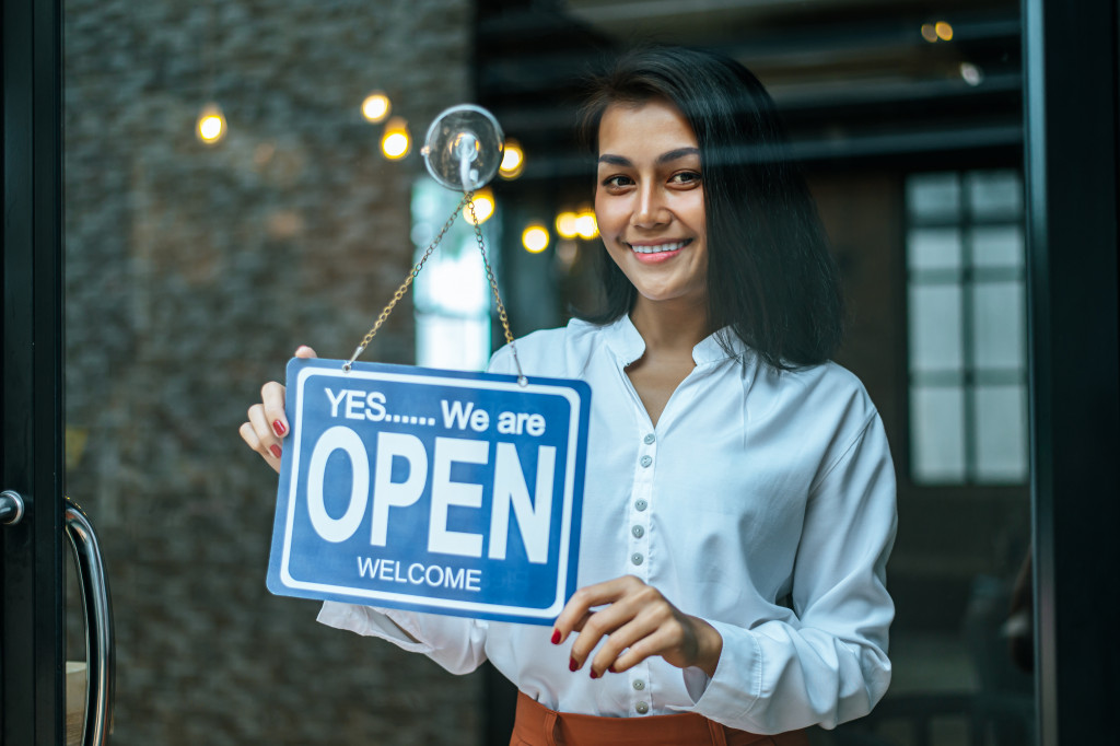 a young woman holding the open sign in a store door