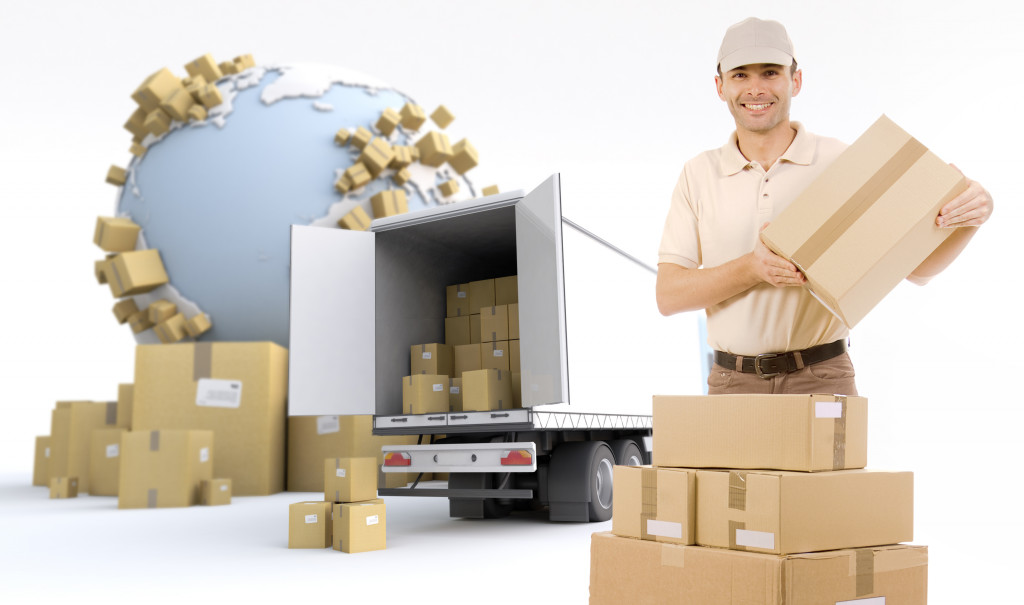 a logistics worker holding a box with stacks of boxes and truck behind with a globe