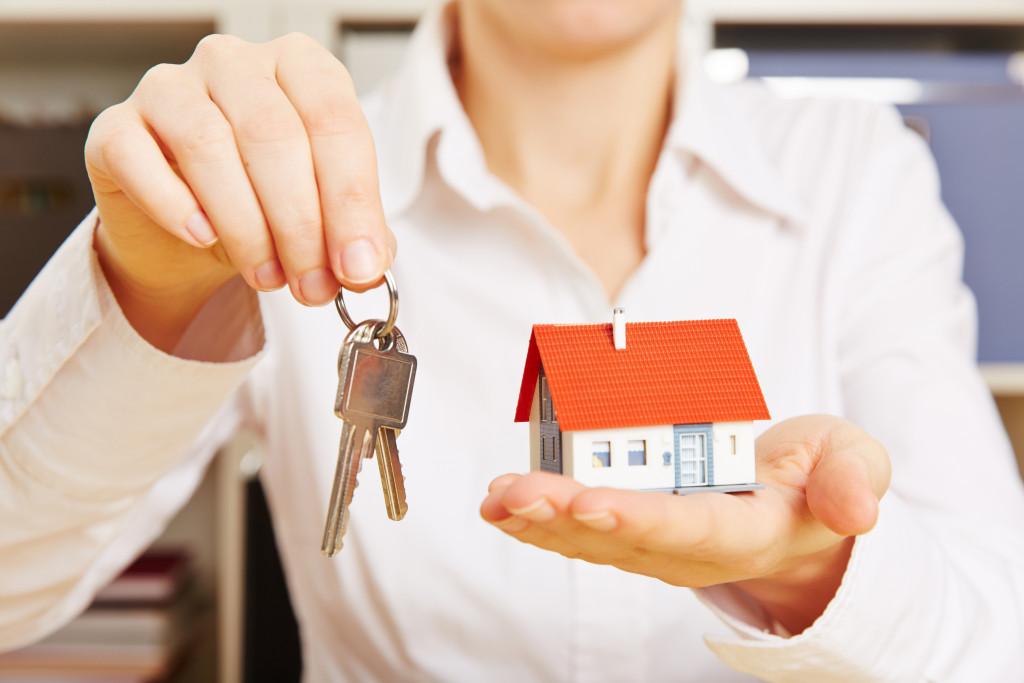 woman handing over house key while holding miniature house model in other hand