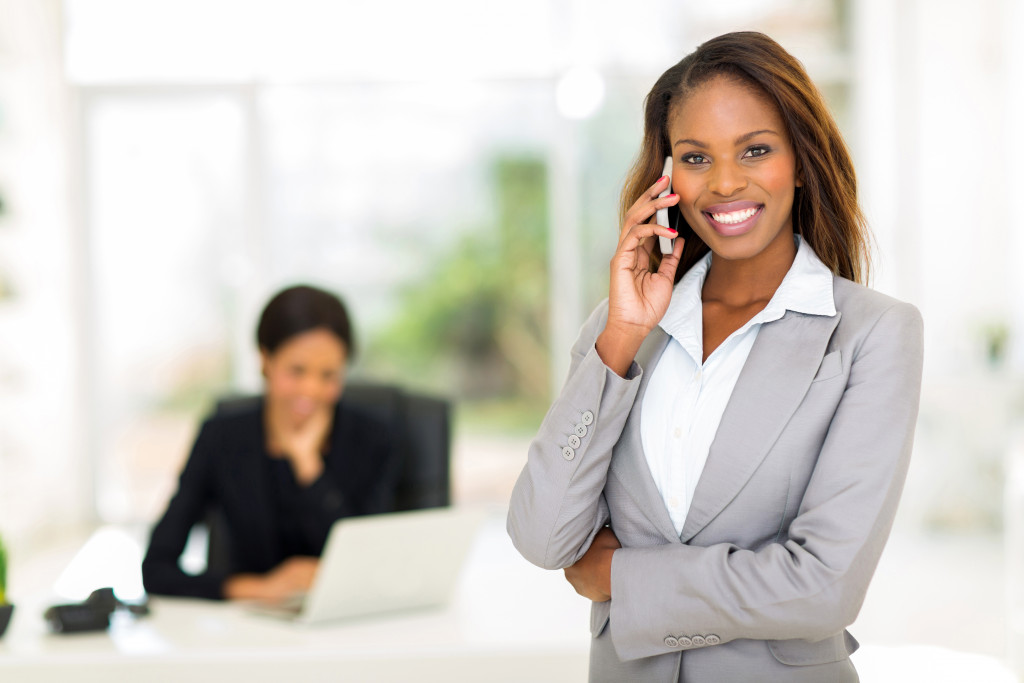 female boss smiling while talking to someone on the phone and a female employee behind her