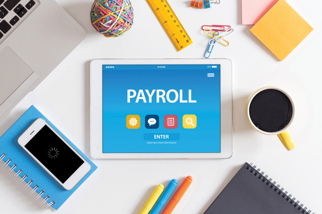 Payroll software on a tablet placed on a table with office supplies.