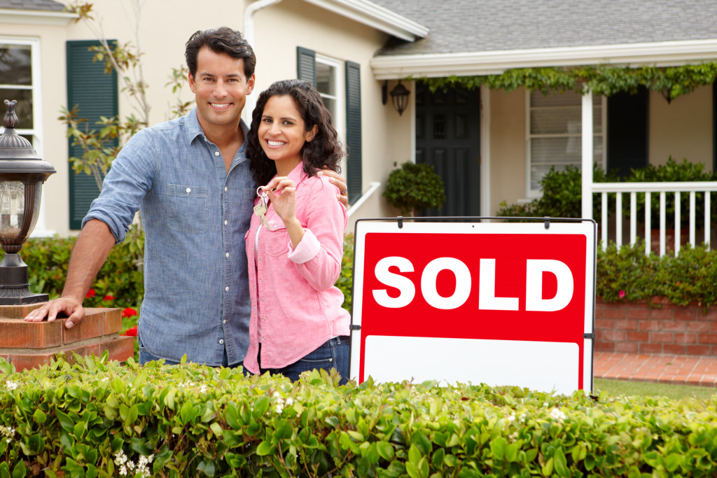 Young couple standing outside a house with a sold sign in front of them.